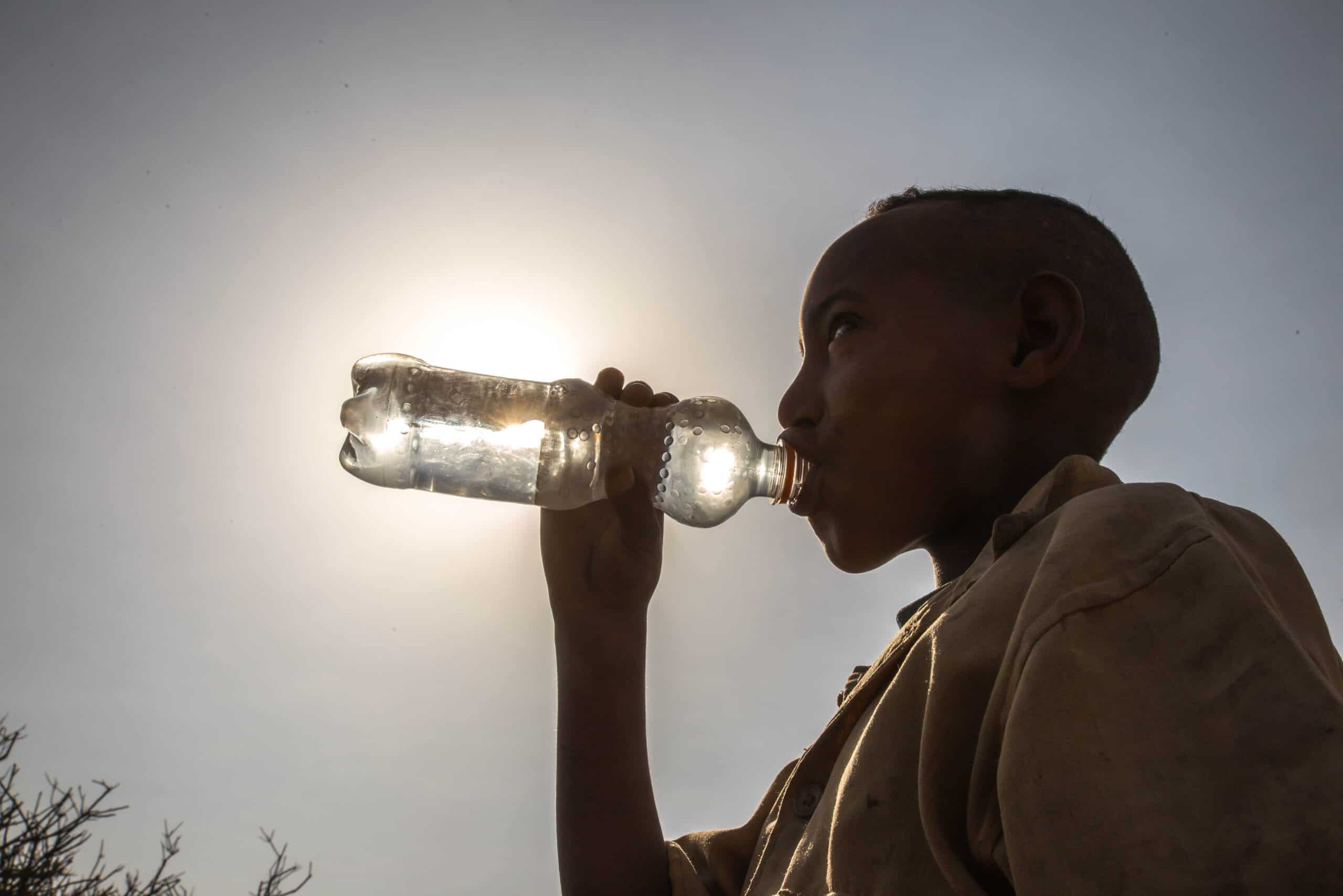Image of boy drinking bottled water against the sun