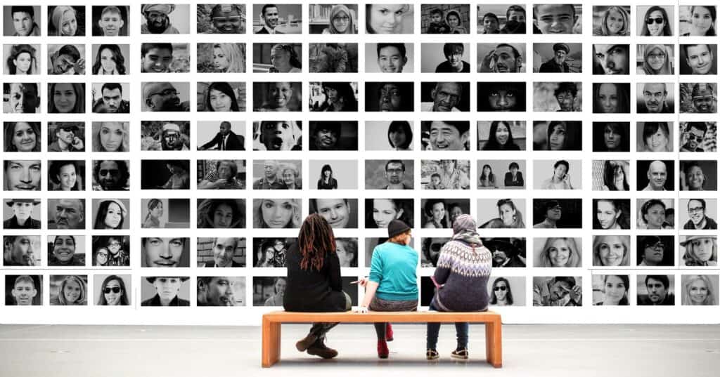 Three people on a bench looking at a wall made up of the faces of lots of different people.