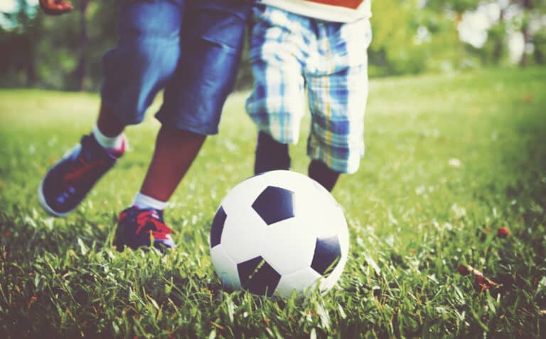 Two children chasing after a football on grass.