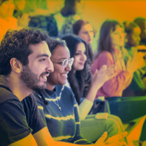 A crowd of students clapping at an event, orange tint over image.