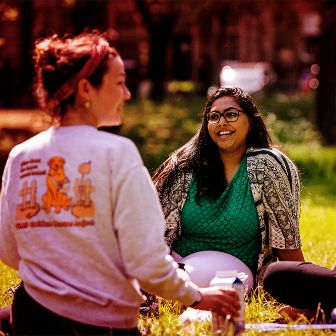 Three female students sitting on the grass in the sun, red tint over image.