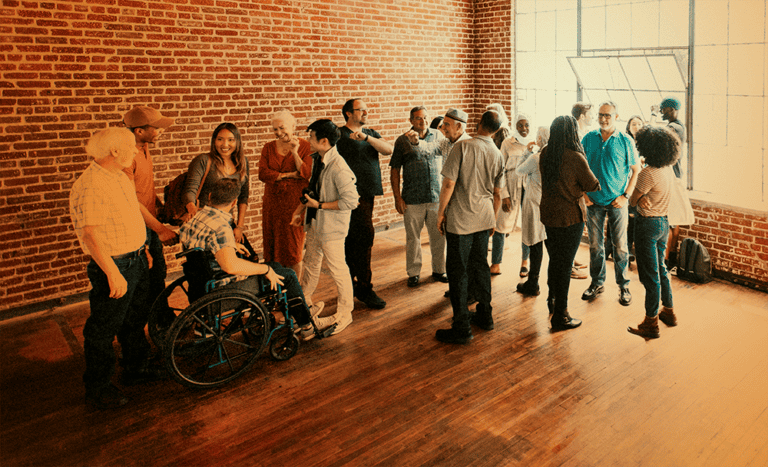 A large group of people meeting in an empty room with bricked walls, orange tint on image.