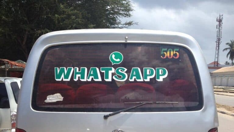 The rear window of a vehicle is shown with a large "WHATSAPP" sticker prominently displayed, along with the app's logo. The number "505" is positioned in colorful digits on the top right of the window. Trees and buildings are faintly visible in the background.