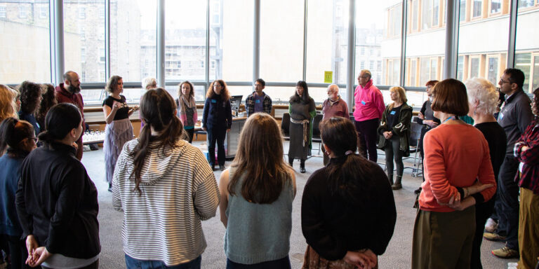 People standing in a circle in a room with large windows behind