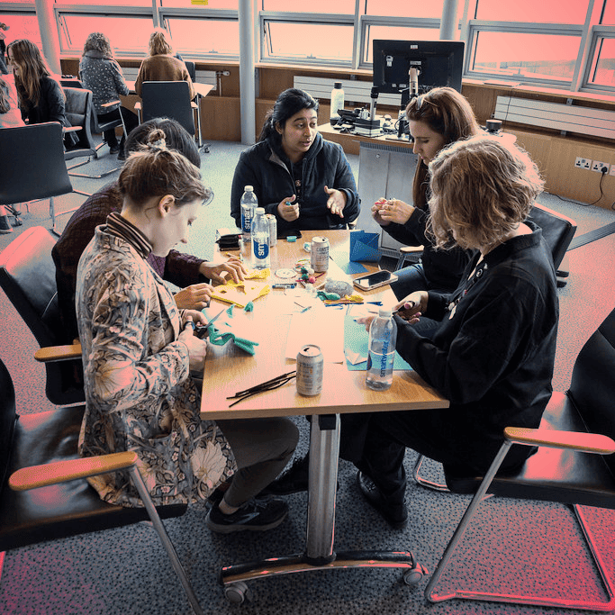 A group of female students sitting at a table doing craftwork, red tint over image.