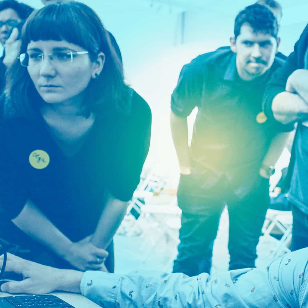 A group of students working collaboratively around a computer, with a blue tint over the image.
