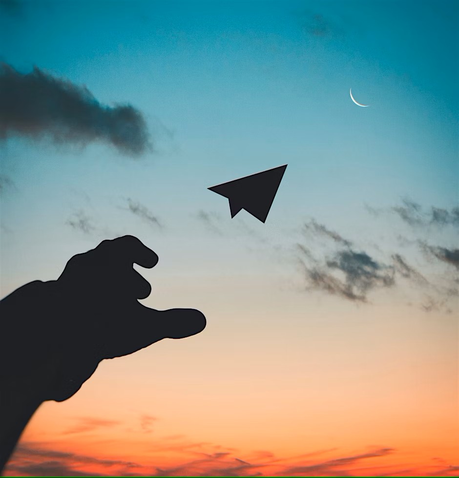 A silhouette of a hand launching a paper airplane into a colorful sunset sky, with a crescent moon and a few clouds visible in the background.