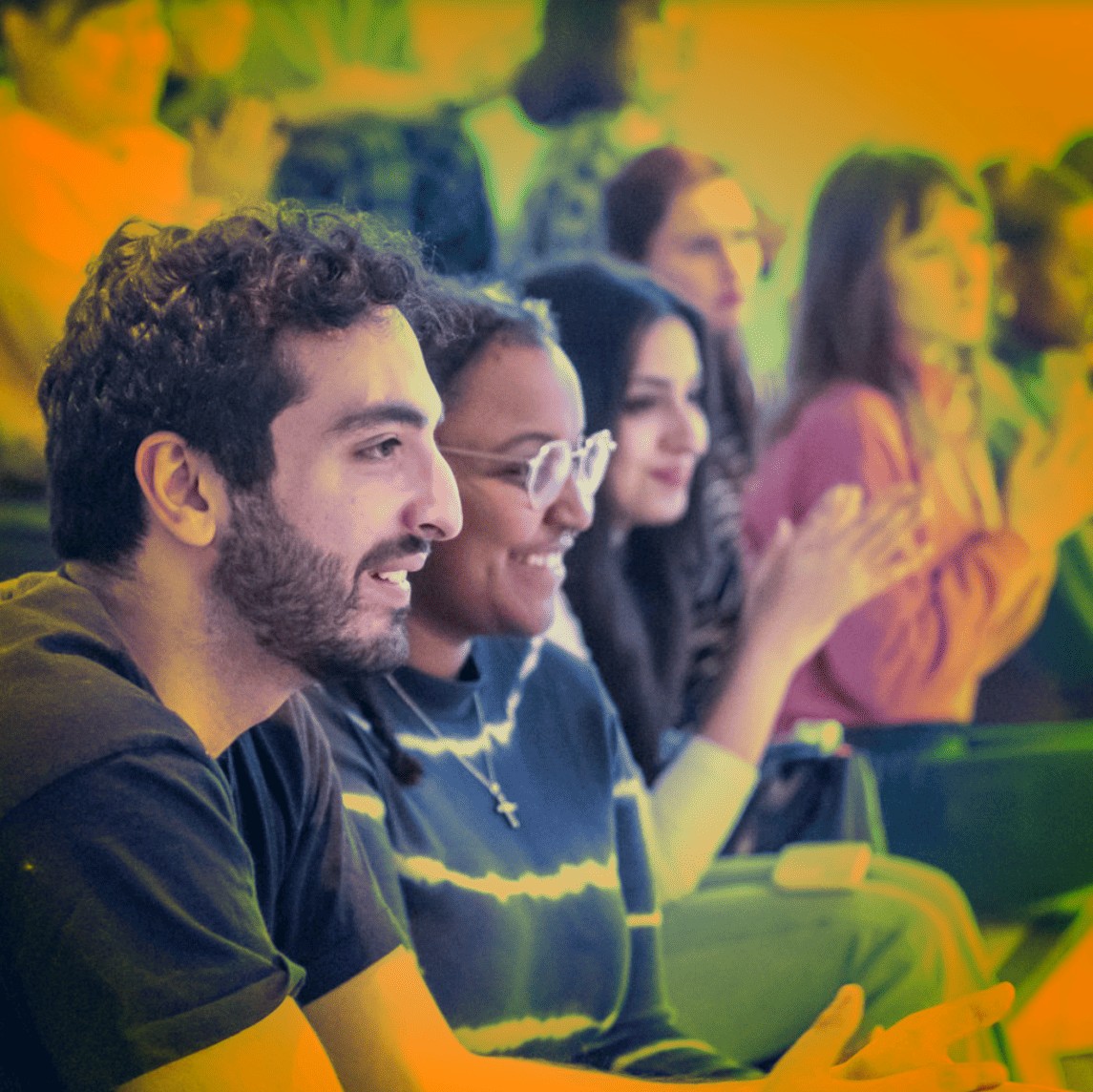 A crowd of students clapping at an event, orange tint over image.