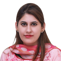 A woman with straight brown hair wearing a pink patterned scarf and top, looking at the camera with a neutral expression against a white background.