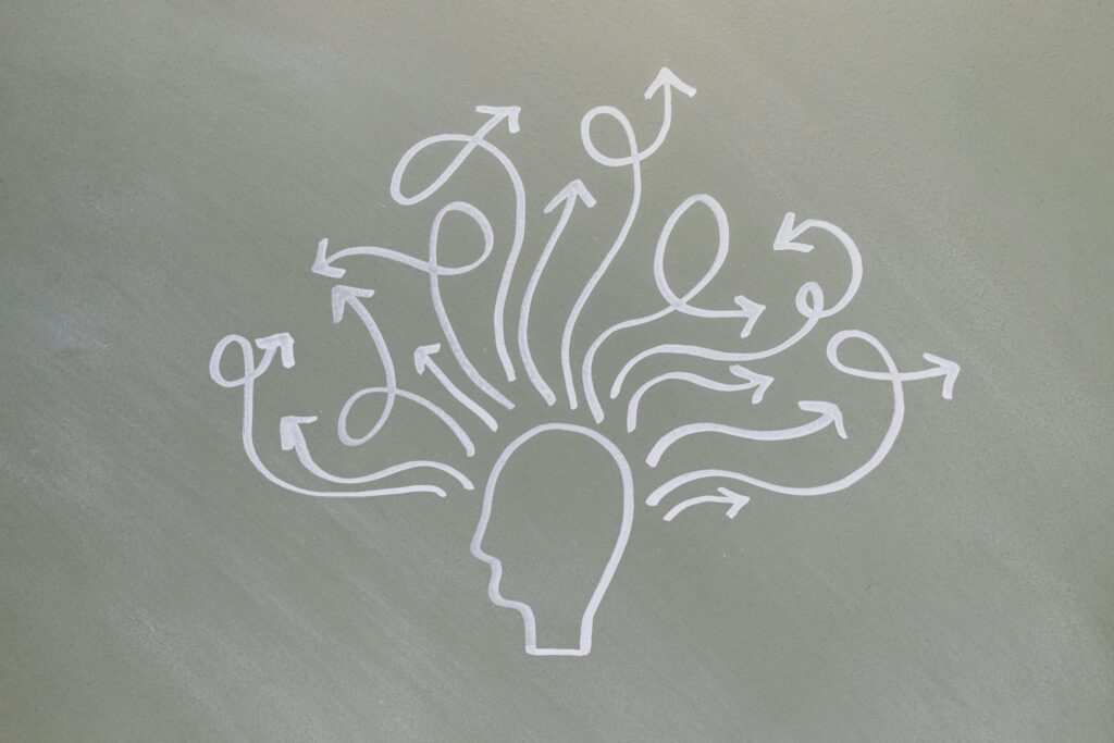 White outline of a human head on a grey background, with multiple arrows emerging from the head and curving in various directions, symbolizing thoughts, ideas, or decision-making.