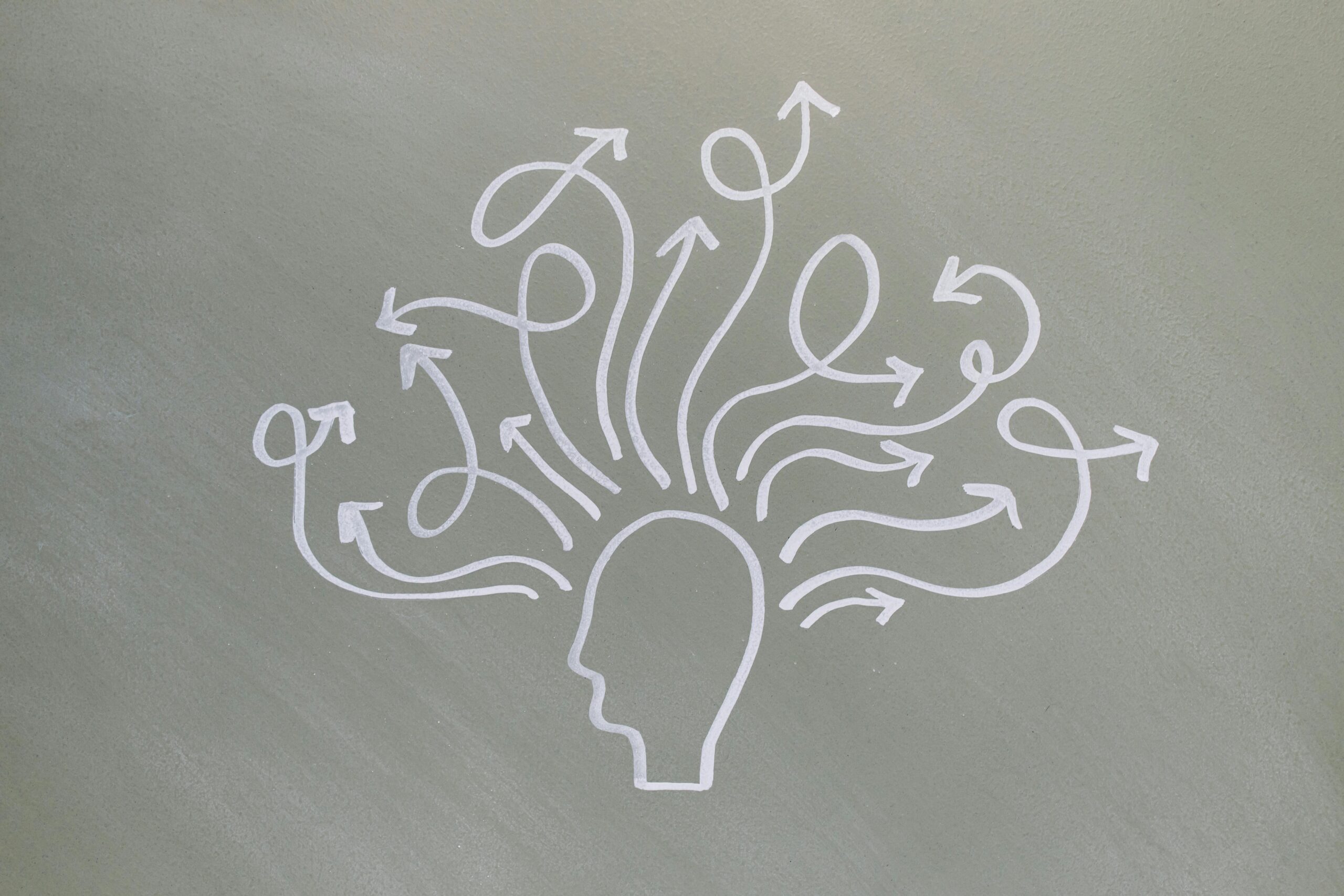 White outline of a human head on a grey background, with multiple arrows emerging from the head and curving in various directions, symbolizing thoughts, ideas, or decision-making.