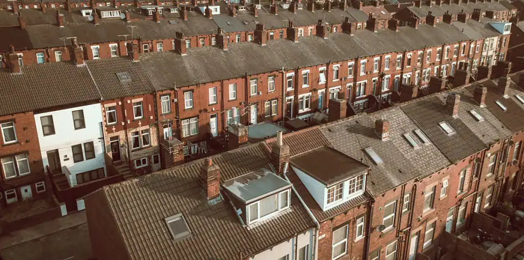 Aerial view of rows of red brick terraced houses with chimneys, closely packed in a residential neighbourhood, bathed in warm sunlight.