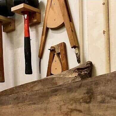 A close-up of a workshop wall with woodworking tools, a plank of reclaimed timber, and the words "Recycling a Hospital" handwritten on a white surface.